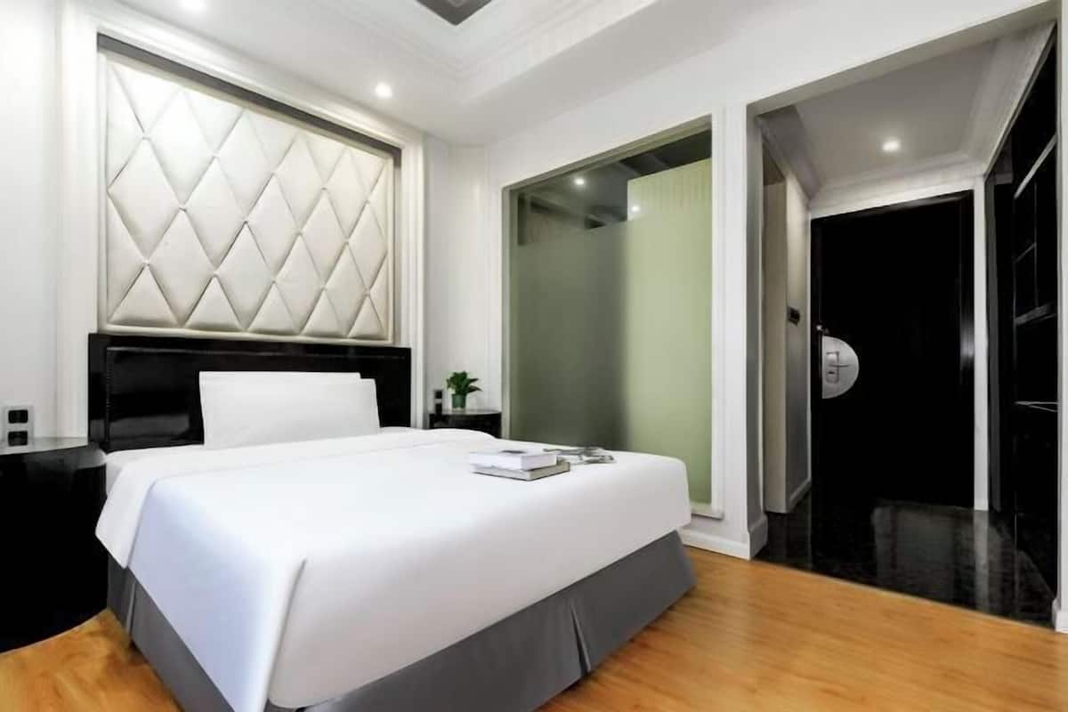 Een moderne hotelkamer met een groot bed, een hoofdeinde met een geometrisch patroon, een nachtkastje en een schuifglazen deur die leidt naar een donkere kamer.