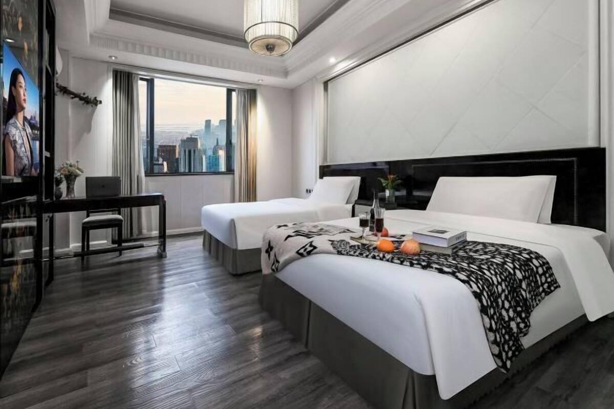 Hotelkamer met uitzicht op de stad, twee bedden, een bureau en een kroonluchter.