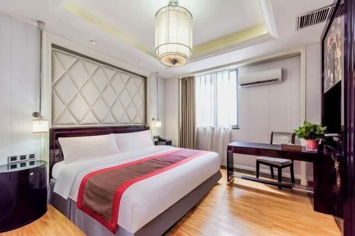 Een hotelkamer met een groot bed, een bureau, een stoel, een bijzettafeltje, een lamp en een plafondlamp.