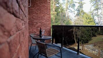 Un balcón con pared de ladrillo, una mesa redonda con dos sillas de mimbre, una botella de vino y una copa.