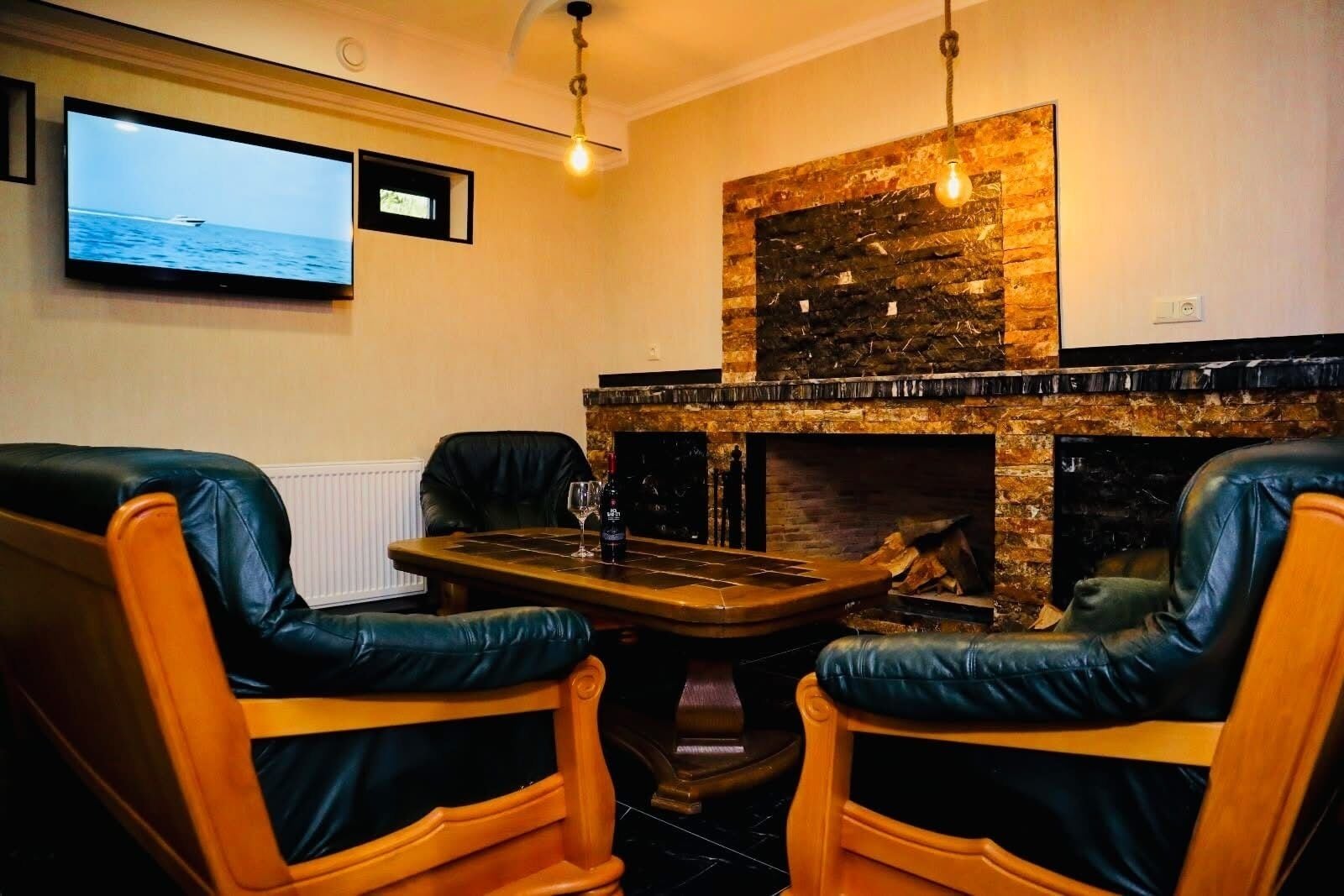 A cozy room with a fireplace, two leather chairs, a table with a bottle and glass, and a TV displaying a boat on the water.