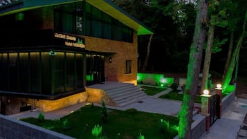 A modern hotel with a glass facade, a green roof, and a well-lit entrance.