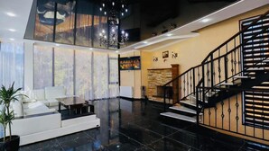 A modern lobby with a white sofa, a staircase, and a chandelier. - Hotel EverGreen (Borjomi)