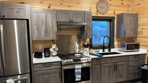 A modern kitchen with stainless steel appliances, wooden cabinets, and a large window with a view of a snowy landscape.