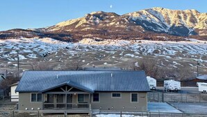 A single-story house with a metal roof, a porch, and a view of snow-covered mountains in the background.
