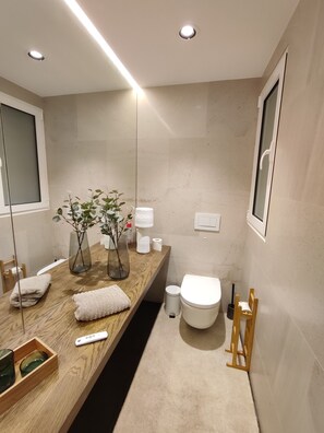 Un baño moderno con tocador de madera, inodoro, bidé y espejo.