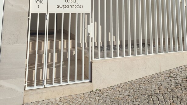 Un edificio moderno con entrada protegida por una reja, identificada con las leyendas 'Lote 1' y 'Casa Superacao'.