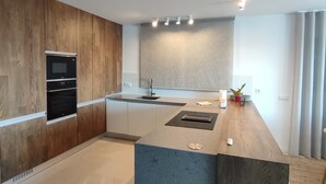 Una cocina moderna con armarios de madera, horno empotrado, una isla grande con pileta e iluminación empotrada en el techo.