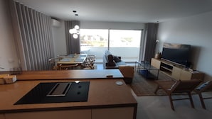 Una sala moderna con comedor, un sofá, un televisor y un balcón con cortinas.