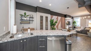 A modern kitchen with a granite countertop, stainless steel appliances, and a built-in dishwasher. - Queen City Views Suites (Cincinnati)