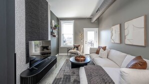 A modern living room with a flat-screen TV, a sofa, a coffee table, and a patterned rug. - Queen City Views Suites (Cincinnati)