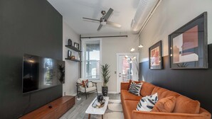 A modern living room with a flat-screen TV, a ceiling fan, a sofa, a coffee table, and framed artwork on the walls. - Queen City Views Suites (Cincinnati)