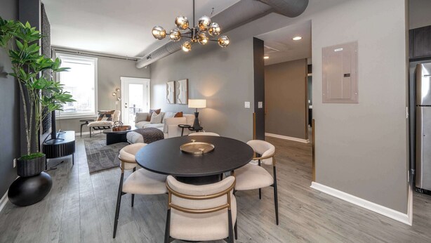 A modern living room with a round dining table, comfortable seating, a large plant, and a stylish chandelier. - Queen City Views Suites (Cincinnati)