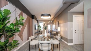 A modern dining area with a glass table and chairs, a hanging light fixture, and a potted plant. - Queen City Views 3 Chic 2 Bdr! (Cincinnati)