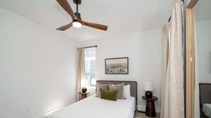A bedroom with a bed, a ceiling fan, a bedside table with a lamp, a window with curtains, and a framed picture on the wall. - Heights on Wayne by Blackhouse (Cincinnati)