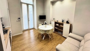 A modern living room with a round dining table, a sofa, and a TV mounted on the wall. - Goa Sea Apartment - Free Parking with Direct Access (Genova)