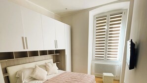 A bedroom with a bed, white cabinets, a radiator, and a window with blinds. - Goa Sea Apartment - Free Parking with Direct Access (Genova)