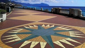 A paved walkway with a star-shaped mosaic design, leading to a waterfront with a railing and a view of the sea and mountains in the background. - Goa Sea Apartment - Free Parking with Direct Access (Genova)