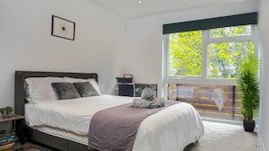 Ein modernes Schlafzimmer mit einem großen Bett, einem Schreibtisch und einem Fenster mit Blick auf Bäume.