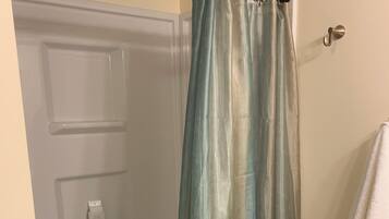 Eine Dusche mit Vorhang, eine weiße Tür, ein Handtuchhalter und ein gemustertes Teppich.
