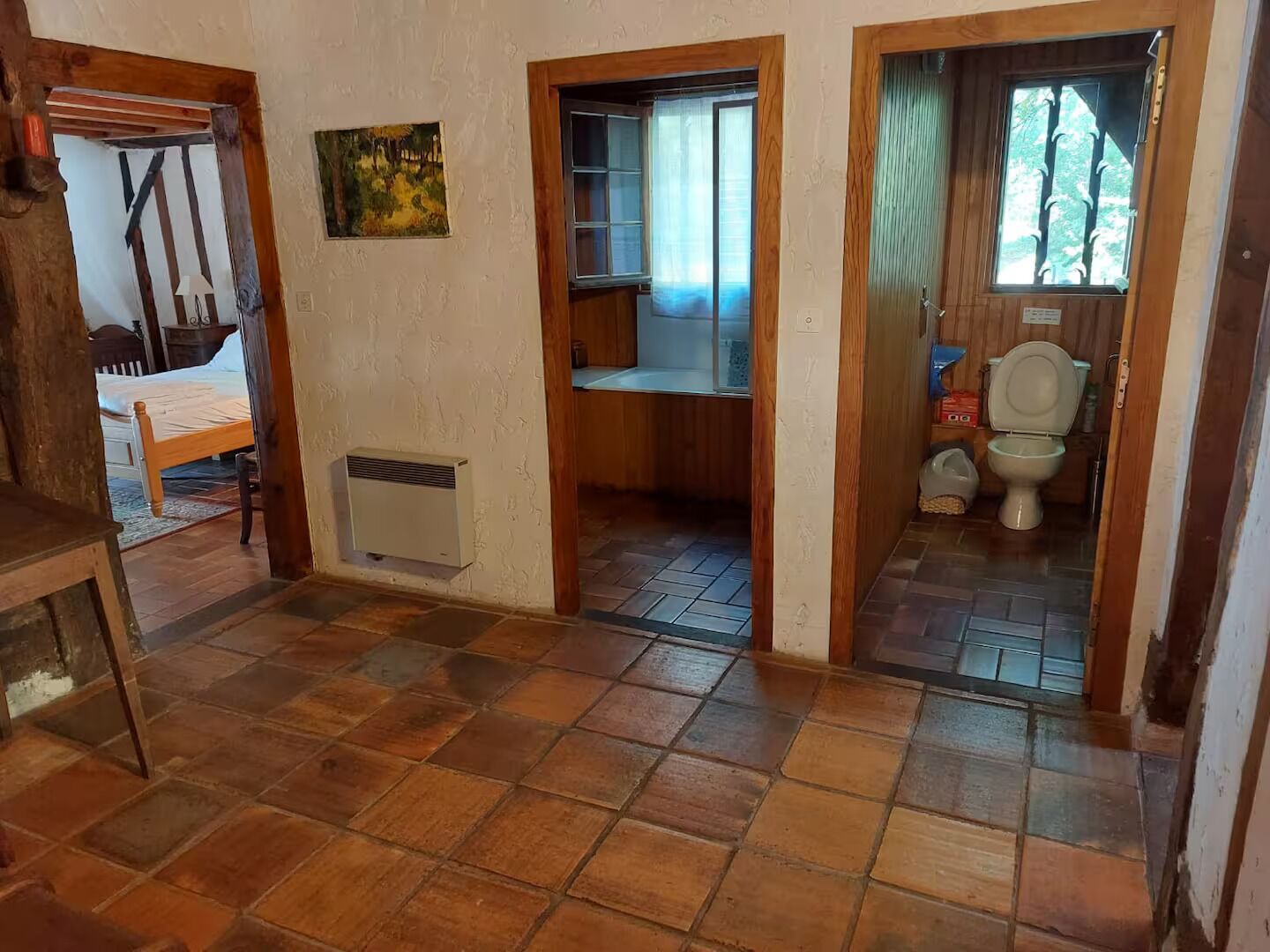 Una habitación con cama, radiador, un cuadro y baño con inodoro y ventana.