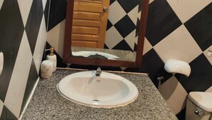 A bathroom with a black and white checkered tile wall, a wooden door, a white sink with a granite countertop, and a toilet. - Patong Rockshore  (Patong)