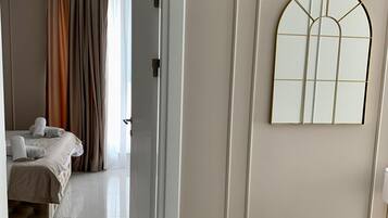 A hotel room with a bed, a bench, a mirror, and a door leading to another room.
