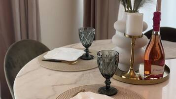A dining table set with two square plates, two glass goblets, a small decorative vase, a bottle, and a tall candle holder.