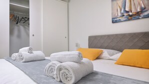 A hotel room with a bed, rolled white towels, a painting of sailboats, and a wardrobe.