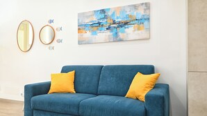 A blue sofa with two yellow cushions, a large abstract painting, and two round mirrors with fish decorations on the wall.