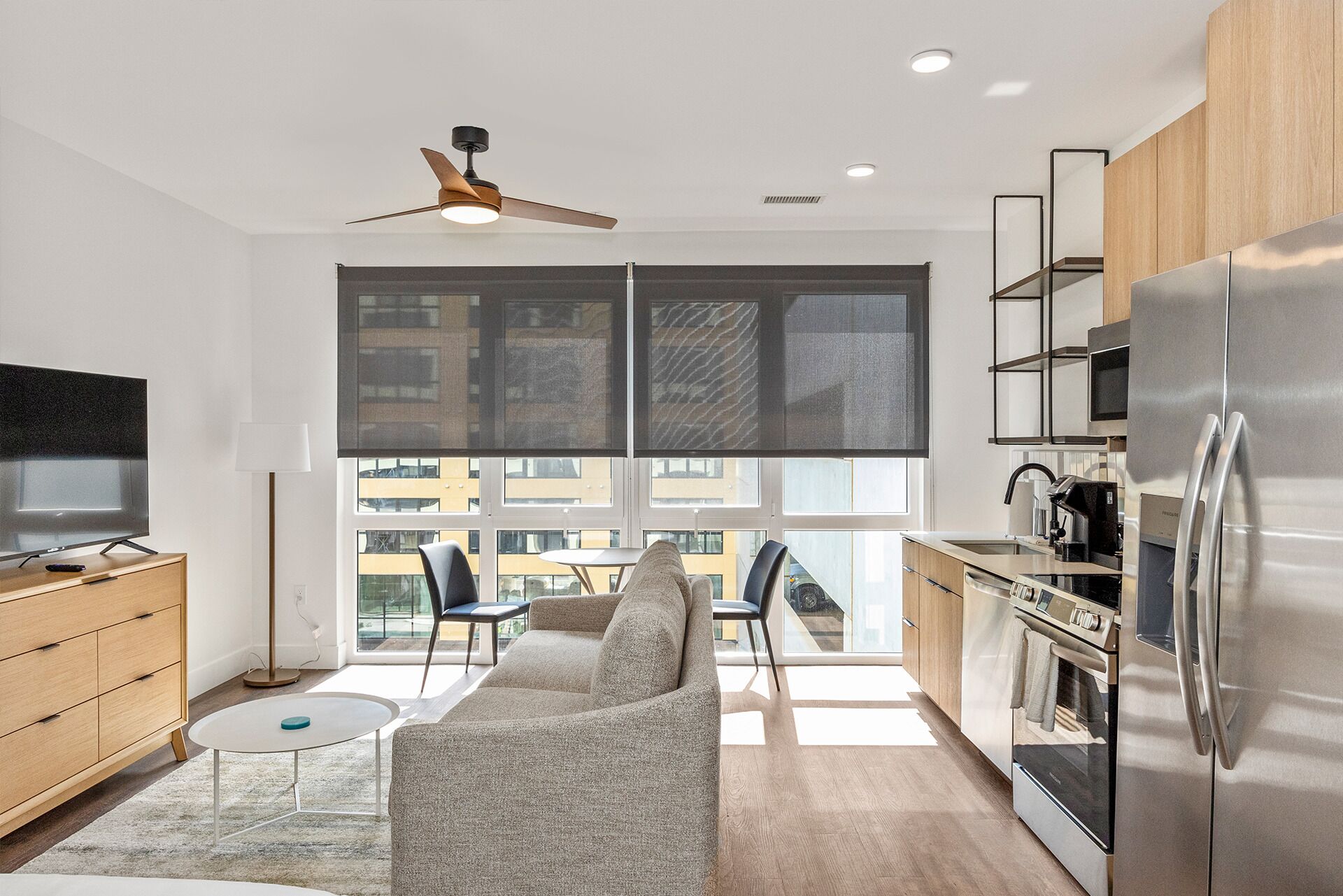 Una cocina moderna con un refrigerador grande, una zona de comedor con un sofá y sillas, y un televisor sobre un mueble de madera.