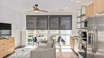 A modern kitchen with a large refrigerator, a dining area with a sofa and chairs, and a TV on a wooden cabinet.