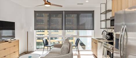 Una cocina moderna con un refrigerador grande, una zona de comedor con un sofá y sillas, y un televisor sobre un mueble de madera.