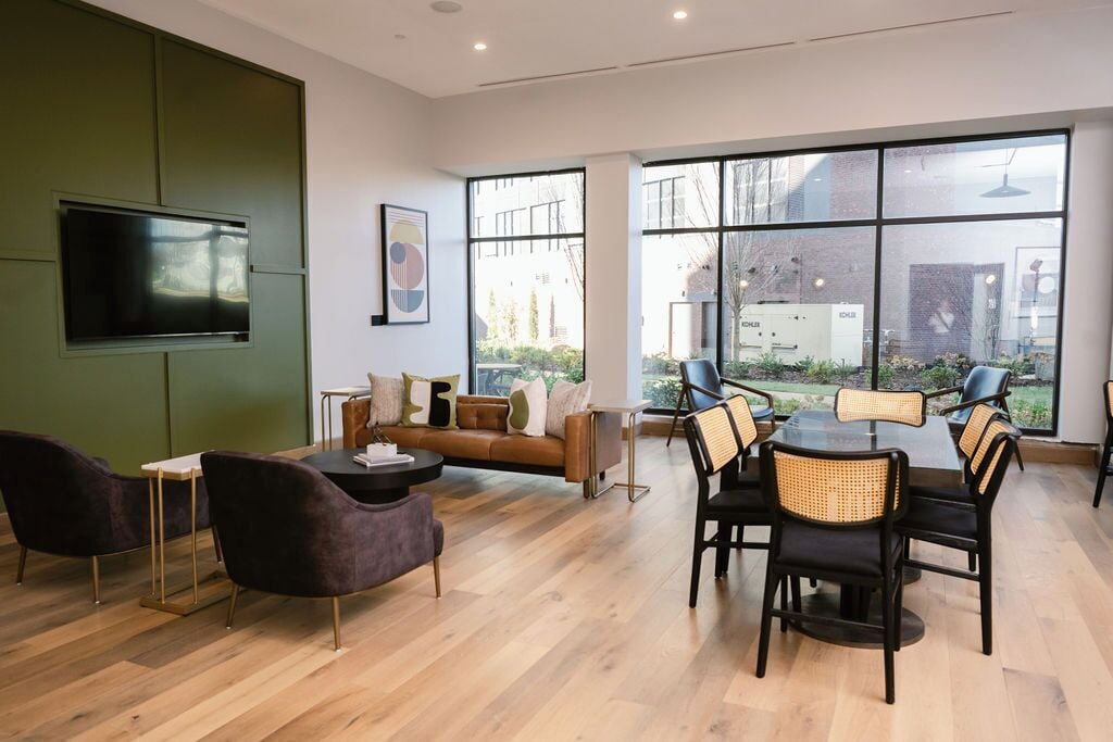 Un interior moderno con un sofá, mesa de comedor, sillas, televisor de pantalla plana y ventanas amplias que ofrecen vistas al exterior.