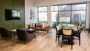 A modern interior with a sofa, dining table, chairs, a flat-screen TV, and large windows offering a view of the outdoors. - Anthem House Huntsville MidCity, powered by Placemakr (Huntsville)