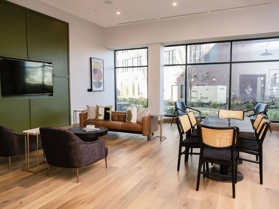 A modern interior with a sofa, dining table, chairs, a flat-screen TV, and large windows offering a view of the outdoors.