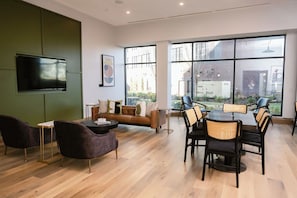 A modern interior with a sofa, dining table, chairs, a flat-screen TV, and large windows offering a view of the outdoors. - Anthem House Huntsville MidCity, powered by Placemakr (Huntsville)