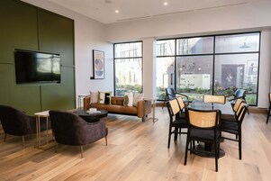 A modern interior with a sofa, dining table, chairs, a flat-screen TV, and large windows offering a view of the outdoors.