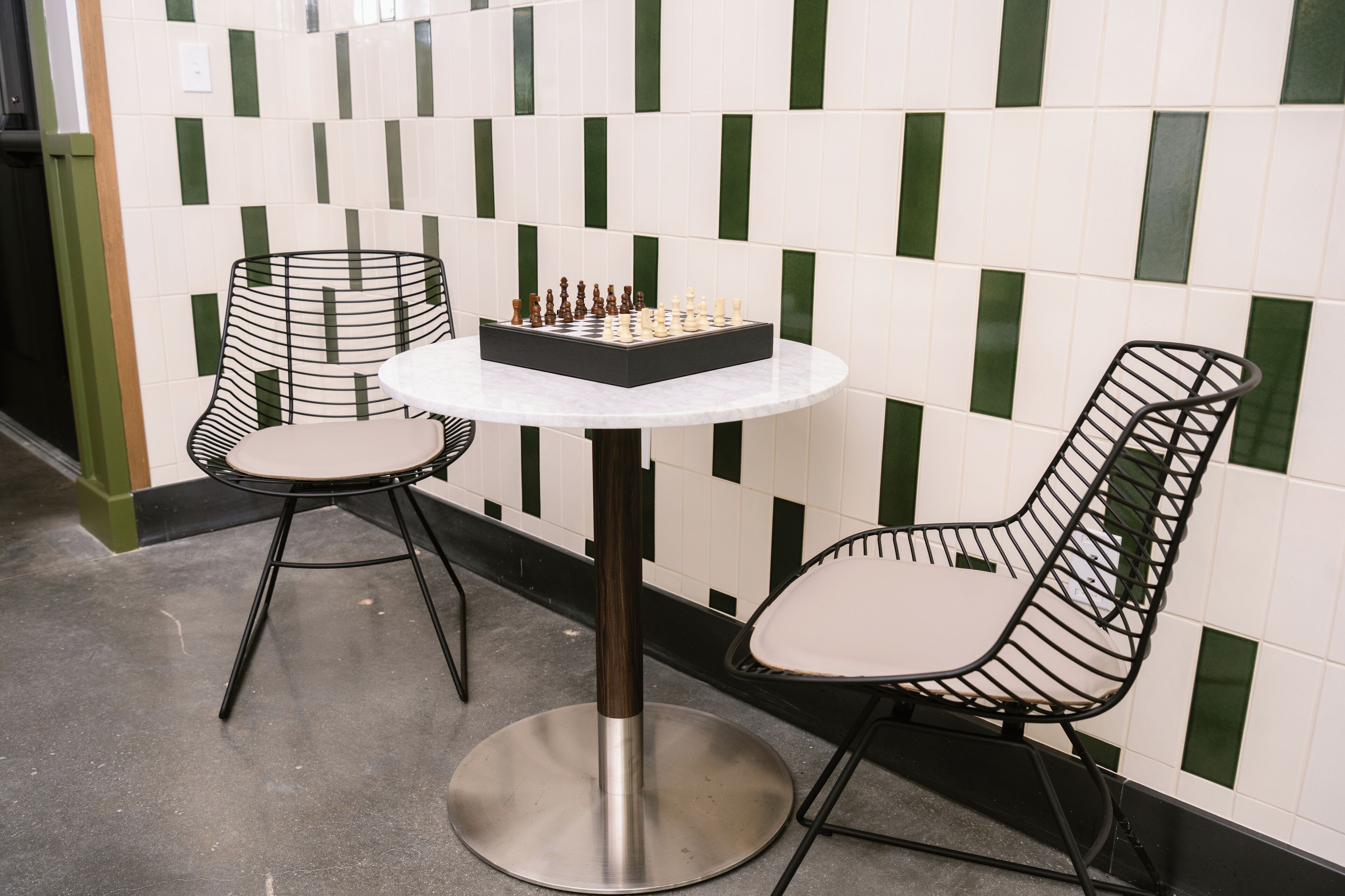 A round table with a chessboard in the center, flanked by two chairs with a unique wireframe design.