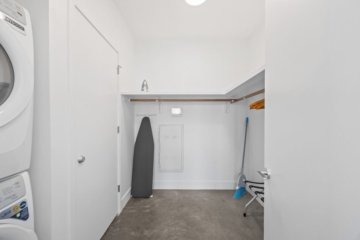 A laundry room with a washing machine, a drying rack, and a broom.