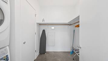 A laundry room with a washing machine, a drying rack, and a broom.