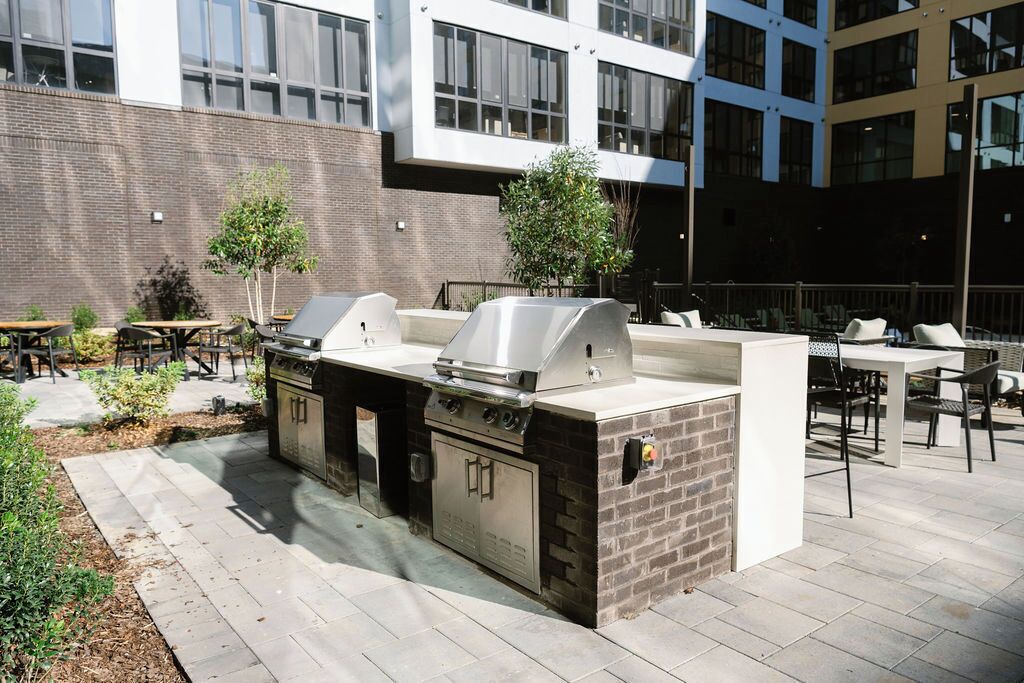 Een terras buiten met een ingebouwde grillplaats, een zithoek en een uitzicht op een modern gebouw op de achtergrond.