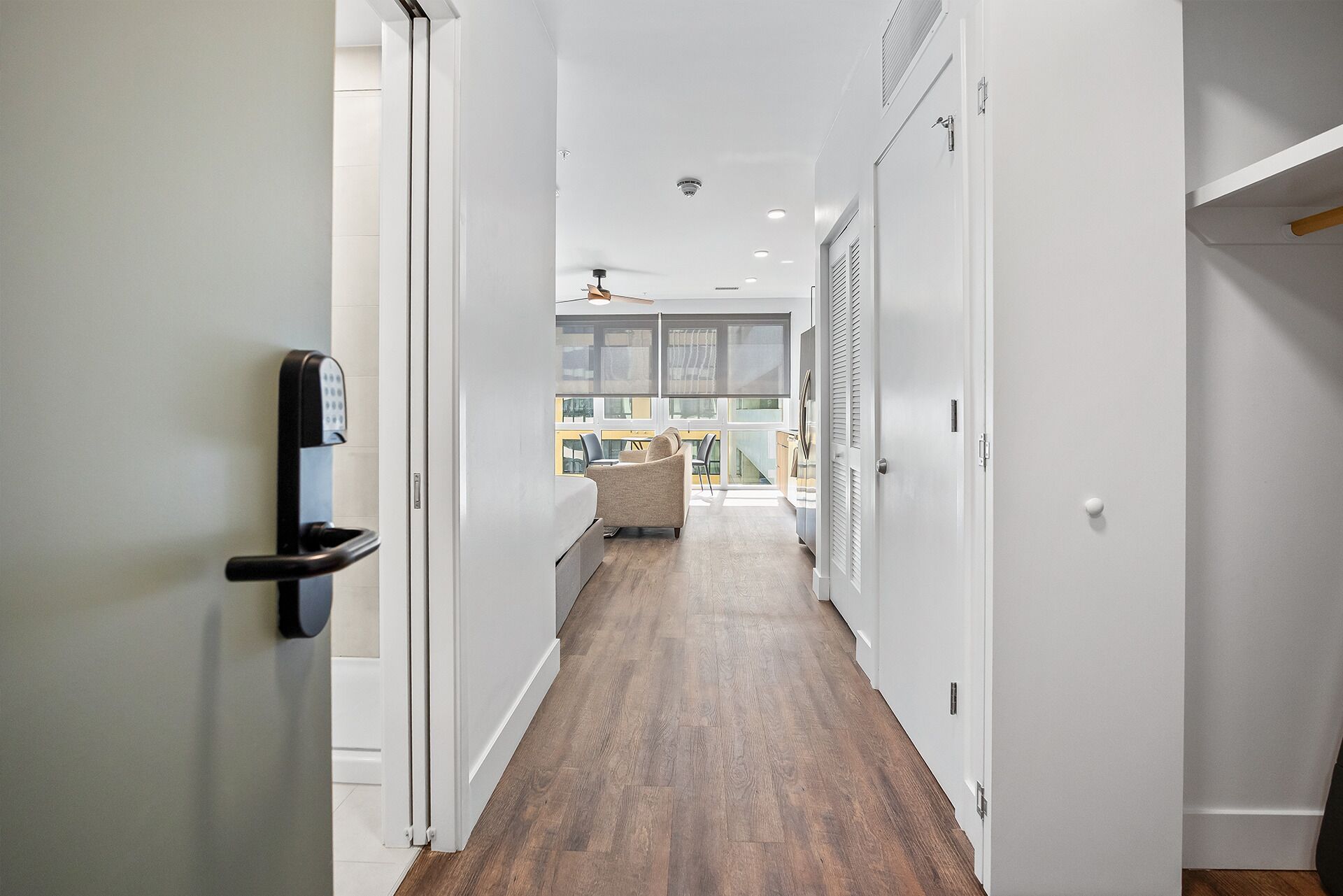A hallway with a wooden floor, white walls, and a door with a keypad lock.