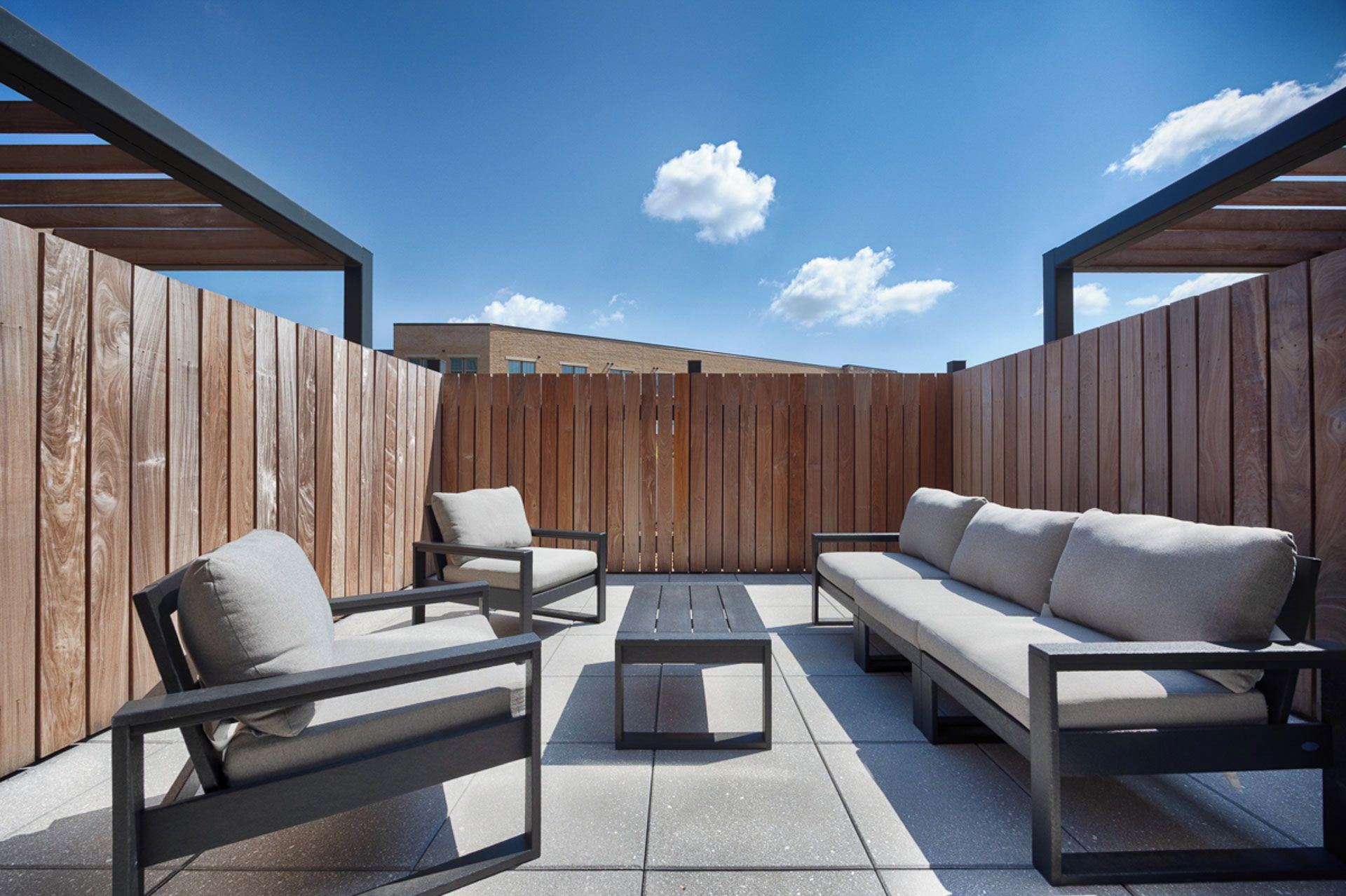 Un patio al aire libre con cerca de madera, un sofá, dos sillas y una mesa de centro.