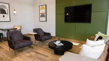 A modern lounge area with two armchairs, a round coffee table, a sofa, and a TV mounted on a green wall.