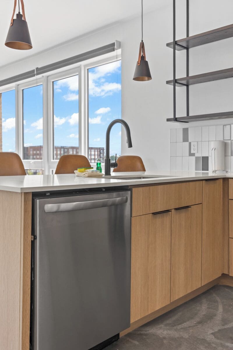 A modern kitchen with a dishwasher, wooden cabinets, a countertop, and pendant lights.