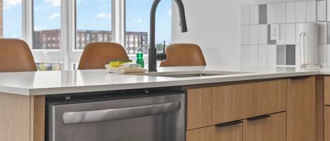 A modern kitchen with a dishwasher, wooden cabinets, a countertop, and pendant lights.