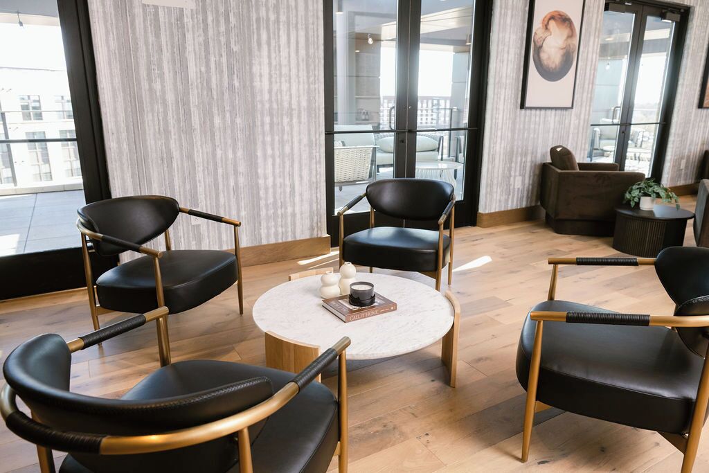 A modern lounge area with black leather chairs, a round coffee table, and a view of the outdoors through large windows.