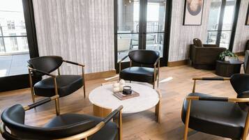 A modern lounge area with black leather chairs, a round coffee table, and a view of the outdoors through large windows.