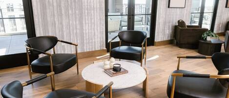 A modern lounge area with black leather chairs, a round coffee table, and a view of the outdoors through large windows.